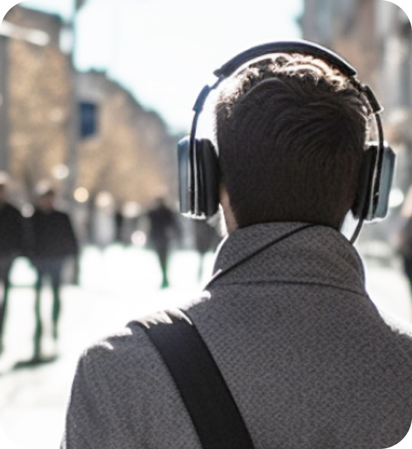 Image looking at the back of a man in a gray wool jacket with headphones on his head. As he is walking down a busy street using the Soundscape Community App.