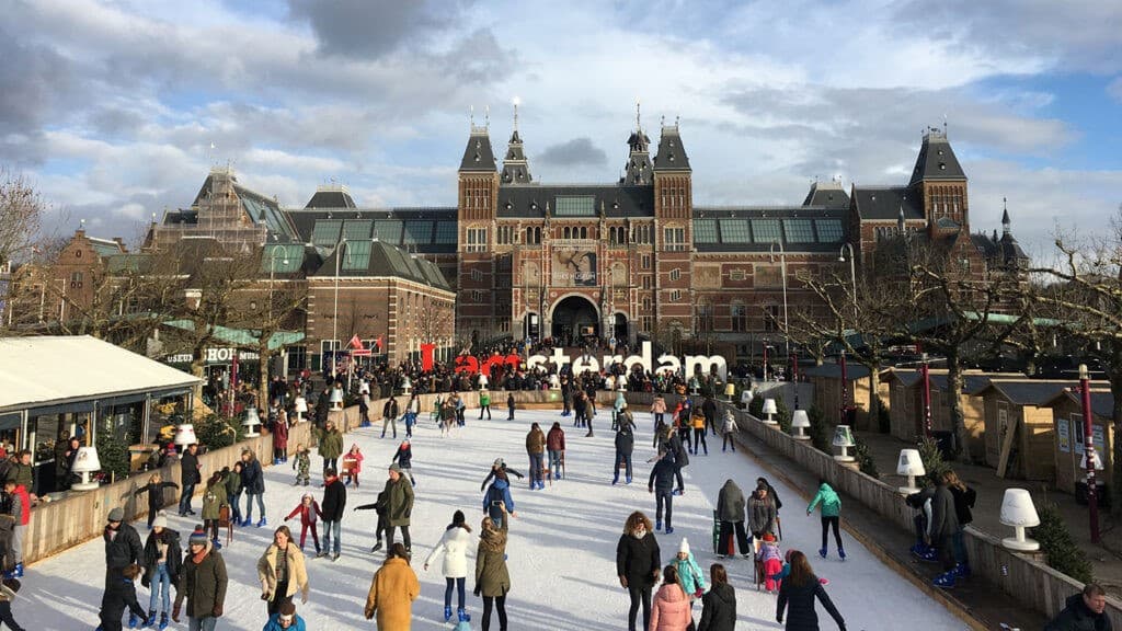 An image of people skating on an ice rink in front of the Amsterdam train station building.